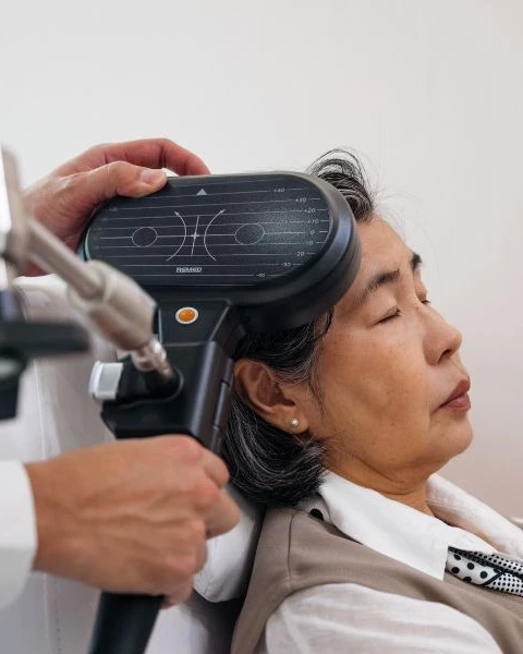 Clinician positioning a TMS coil on a woman's head during treatment