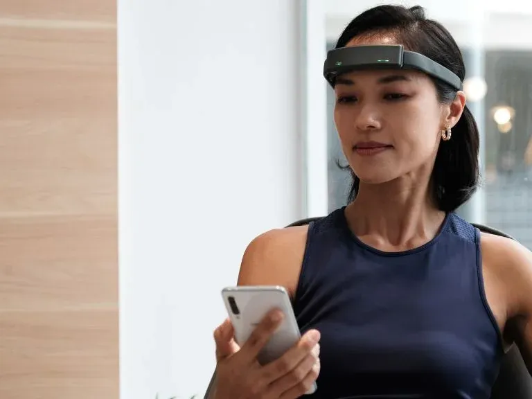 Woman wearing an EEG neurofeedback headband while using a smartphone
